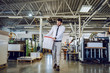 © Dusan Petkovic - Full length of handsome caucasian bearded graphic engineer carrying bucket with liquid glue. Printing shop interior. In background are printing machines.