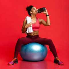 Wall Mural - Athletic girl in sportswear on fitness ball drinking sports food