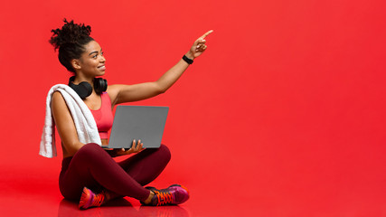 Wall Mural - Smiling fitness girl with laptop pointing up at copy space