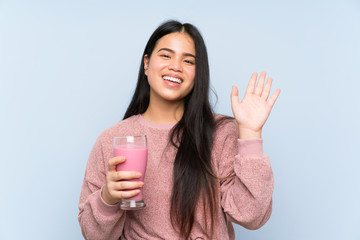 Young teenager Asian girl with strawberry milkshake saluting with hand with happy expression