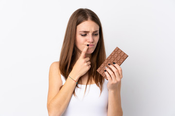 Wall Mural - Young woman over isolated white background taking a chocolate tablet and having doubts