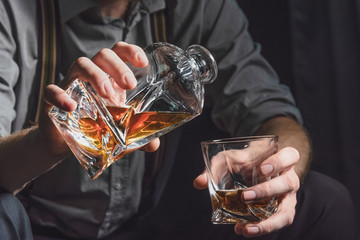 Close-up of the hands of a young man who pours alcohol from a decanter into a glass, on a dark isolated background