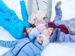 Wall Mural - Beautiful joyful girls in hats and in winter jackets lie on the snow smiling