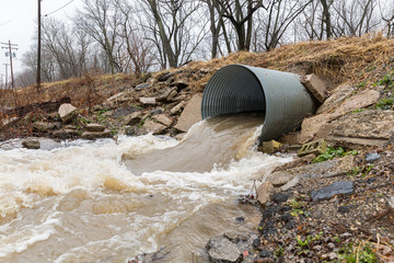 closeup motion blur of storm water runoff flowing through metal drainage culvert under road. january