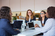 © Mangostar - Content businesswomen discussing work in office. Group of professional multi ethnic businesswomen sitting around table and working with laptops in office. Women in business concept