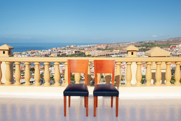 Two red wooden indoor chairs coated with dark leather cushions facing forward and positioned on a top-terrace in a building with view towards the coast and Atlantic, in Tenerife, Canary Islands, Spain