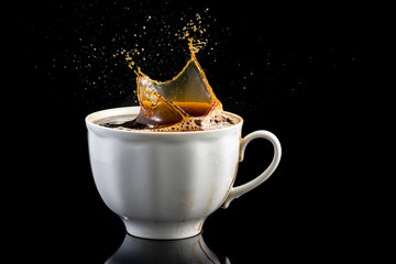 splash and splatter from a piece of sugar in a mug with coffee on a black background