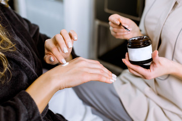 Wall Mural - Allergy test and cosmetology consultation. Cropped image of professional female cosmetologist giving cream for her client hand while testing it for allergy. Woman client applying cream on her hand