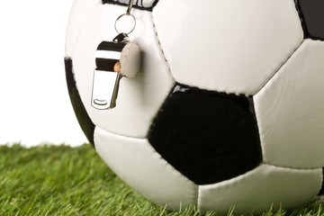 Poster - Single black and white soccer sports ball with referee whistle close up with selective focus on green grass over white