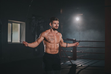 Details of a athletic guy using a cross jumping rope to do his hard training workout exercises in a dark gym class