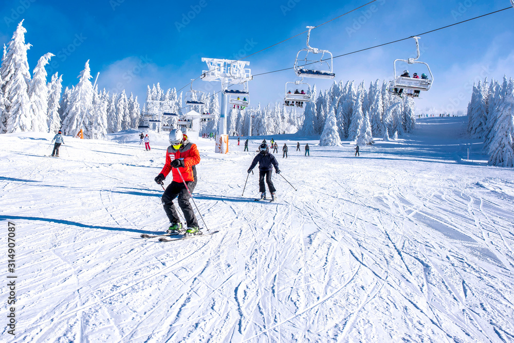 People enjoying skiing and snowboarding in mountain ski resort with beautiful winter landscape in the background - obrazy, fototapety, plakaty 