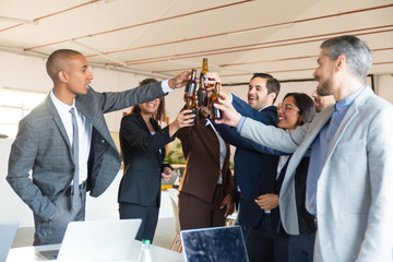 Joyful office managers cheering with beer bottles. Cheerful young people relaxing after hard work. Relaxation concept