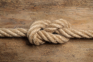 Linen rope with knot on wooden background, closeup. Unity concept