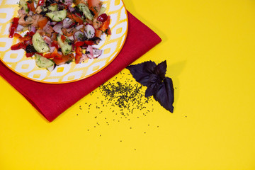 Canvas Print - Dry basil seeds, fresh basil leaves, vegetable salad in colorful plate on red textile cover on yellow background