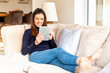 © gzorgz - Happy woman using digital tablet while relaxing at home on the sofa