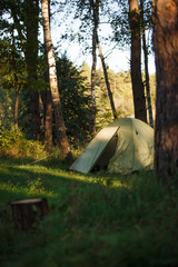 a green tourist tent stands in the forest, illuminated by rays of light. setting up a tent in a tour