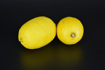 Large, ripe bright yellow two lemons lie on a black plastic background. Delicious and sour fruits, healthy food for every day.