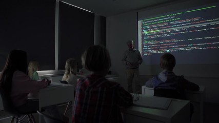 tilt down view of mature teacher talking to audience while teaching kids programming during computer