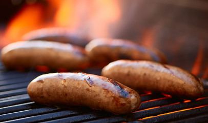 grilling bratwurst sausages over flaming grill