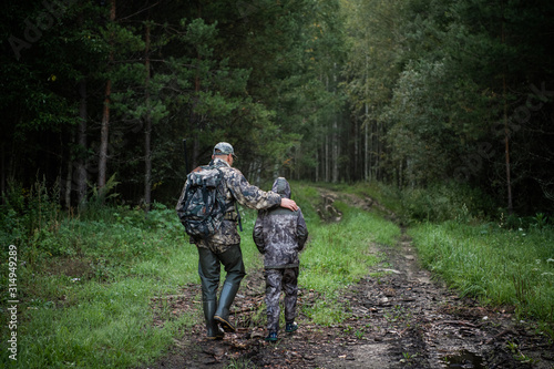 Photographie Hunters with hunting equipment going away through rural field towards forest at sunset during hunting season in countryside