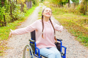 Young happy handicap woman in wheelchair on road in hospital park enjoying freedom. Paralyzed girl in invalid chair for disabled people outdoor in nature. Rehabilitation concept.