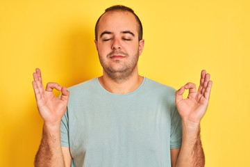 Sticker - Young man wearing green casual t-shirt standing over isolated yellow background relax and smiling with eyes closed doing meditation gesture with fingers. Yoga concept.