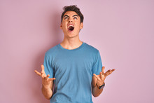 Teenager Boy Wearing Casual T-shirt Standing Over Blue Isolated Background Crazy And Mad Shouting And Yelling With Aggressive Expression And Arms Raised. Frustration Concept.