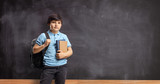 Fototapeta Łazienka - Kid with a backpack and books standing in front of a blackboard