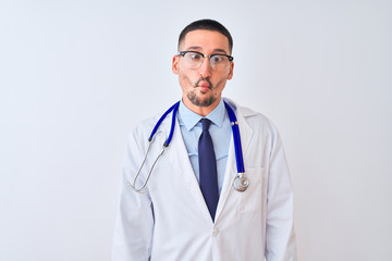 Wall Mural - Young doctor man wearing stethoscope over isolated background making fish face with lips, crazy and comical gesture. Funny expression.