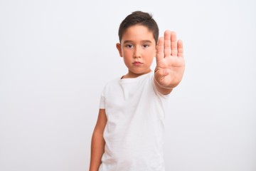 Sticker - Beautiful kid boy wearing casual t-shirt standing over isolated white background doing stop sing with palm of the hand. Warning expression with negative and serious gesture on the face.