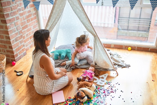 Fotomural Beautiful teacher and blond toddler girl playing with dolls inside tipi at kinde