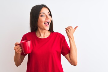 Wall Mural - Young beautiful woman drinking red cup of coffee standing over isolated white background pointing and showing with thumb up to the side with happy face smiling
