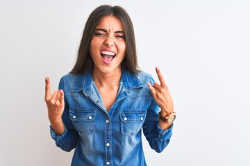 Wall Mural - Young beautiful woman wearing casual denim shirt standing over isolated white background shouting with crazy expression doing rock symbol with hands up. Music star. Heavy concept.