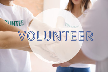 Wall Mural - Team of young volunteers putting hands together indoors