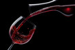 Red wine is poured into a wine glass on a black background.