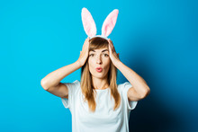 Young Woman In Bunny Ears With A Surprised Face On A Blue Background. Easter Concept