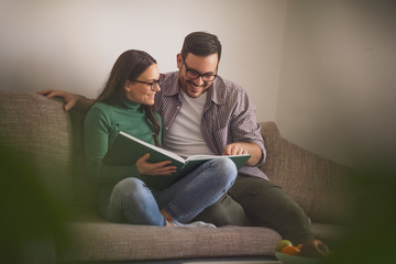 Wall Mural - Happy couple is sitting at sofa in their home and looking at book.