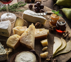 Wall Mural - Cheese platter with organic cheeses, fruits, nuts and wine on wooden background. Top view. Tasty cheese starter.