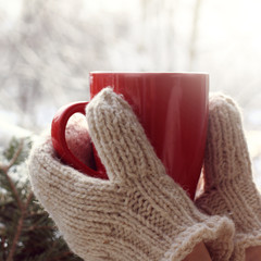 Wall Mural - red mug in hands dressed in white knitted mittens on a background of a winter landscape. warming atmosphere of a frosty morning