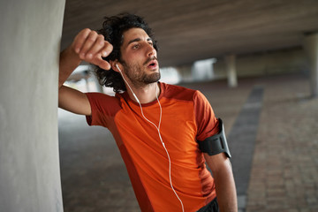 Wall Mural - Portrait of a fitness athlete man in earphone breathing heavily after running and doing exercise - exhausted athlete runner