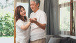 © tirachard - Asian elderly couple dancing together while listen to music in living room at home, sweet couple enjoy love moment while having fun when relaxed at home. Lifestyle senior family relax at home concept.