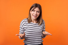 What Do You Want? Portrait Of Confused Annoyed Woman With Brown Hair In Long Sleeve Shirt Raising Arms, Asking And Having No Idea What Happening. Indoor Studio Shot Isolated On Orange Background
