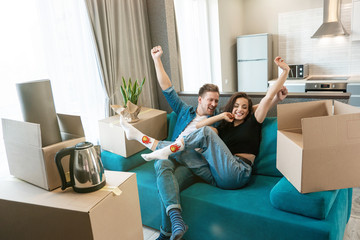 Wall Mural - young couple man and woman looking happy having break on the sofa with hands up in the air during moving to new appartment unpacking boxes