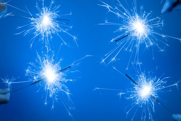 Close up of Bright burning four sparklers in hands on a blue background.