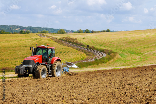 Fotografía Farmer in red tractor preparing land with plow for sowing