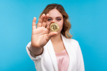 Cryptocurrency. Portrait Of Young Woman With Wavy Hair In White Jacket Holding Physical Golden Bitcoin, Advertising Of Btc Crypto Coin, Digital Currency. Indoor Studio Shot Isolated On Blue Background