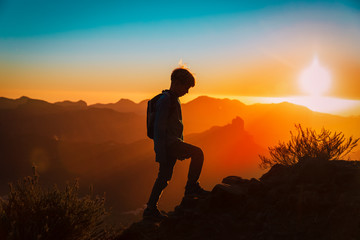 Wall Mural - Silhouettes of young boy hiking at sunset mountains