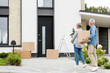 © LIGHTFIELD STUDIOS - mature man holding box and woman holding plant near new house