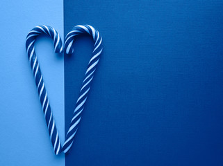 Sweet striped candy canes in the shape of a heart on classic blue tinted two-tone background top view with copy space for your text. Valentines day, love, romance concept.