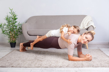 cheerful mother doing plank workout with little daughter on her back, having fun smiling at camera, 